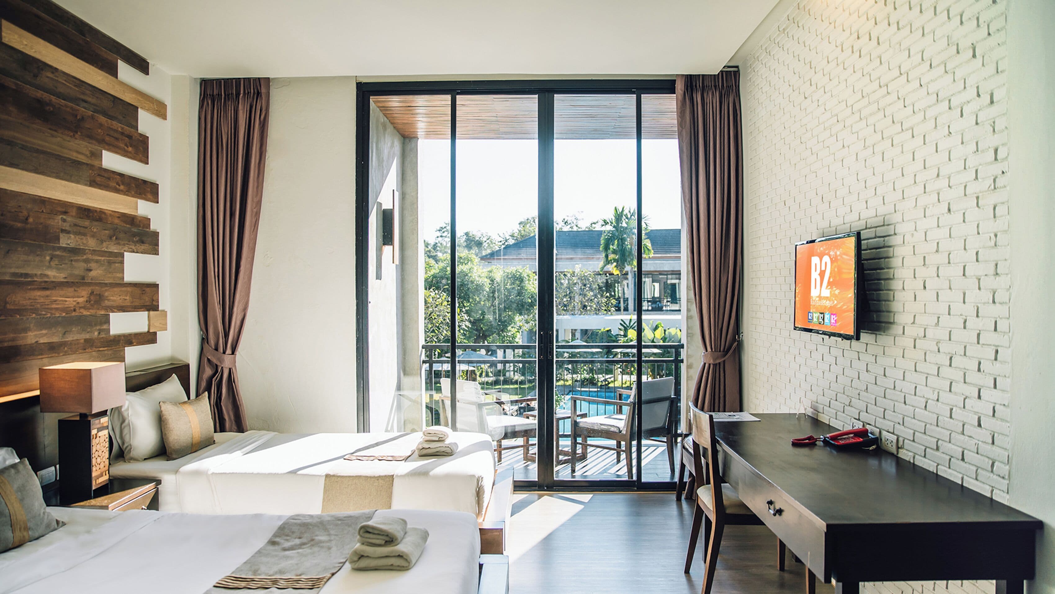 A hotel room with a bed, a desk, a TV, and a balcony with a pool view.