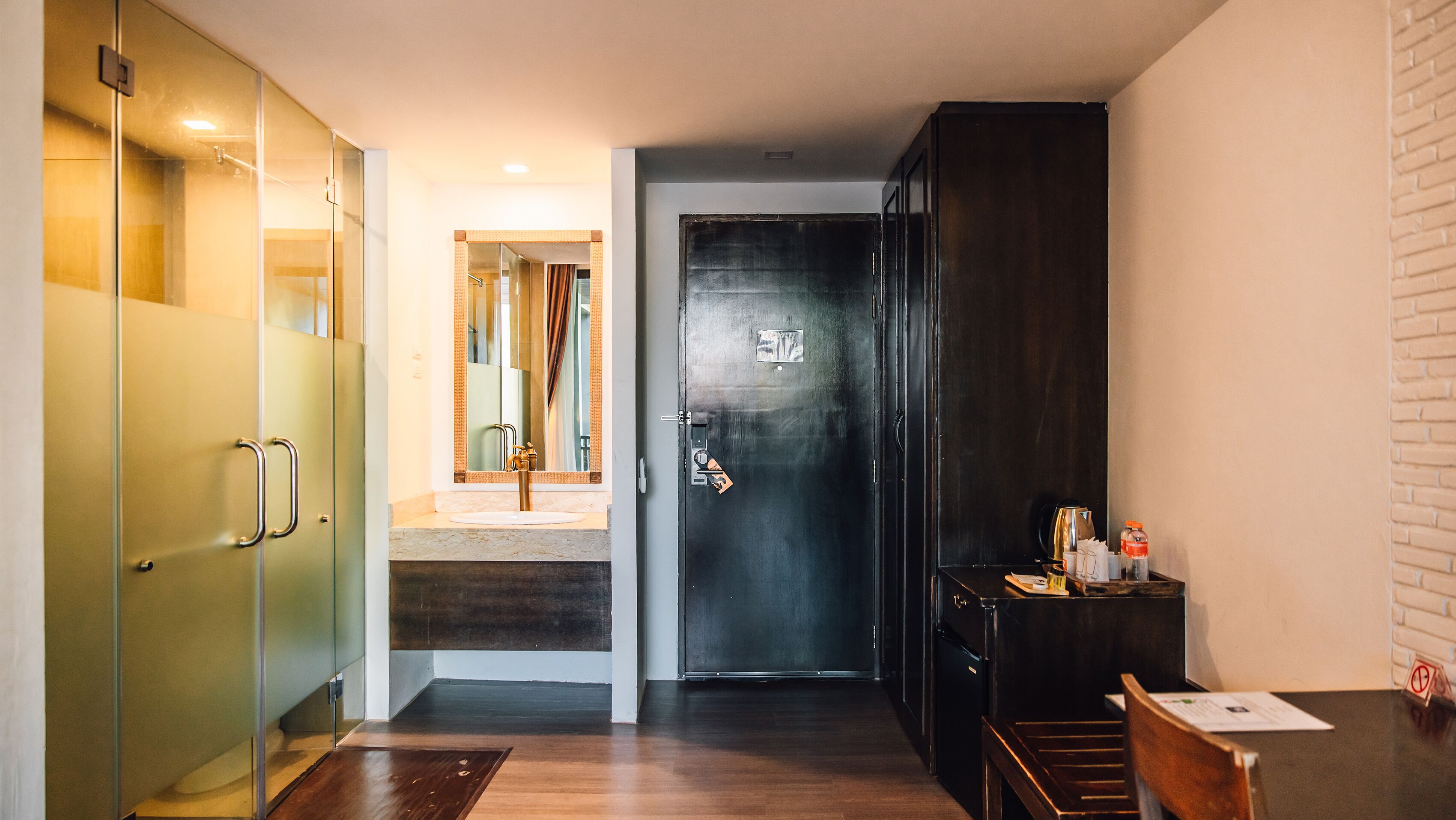 Pasillo de hotel con cabina de ducha de vidrio, una puerta de madera oscura y una pequeña mesa con una silla.