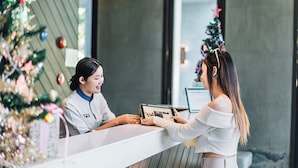 A reception desk with a person holding a tablet, a Christmas tree in the background, and a modern interior design. - B2 Pai Premier Resort (Pai)