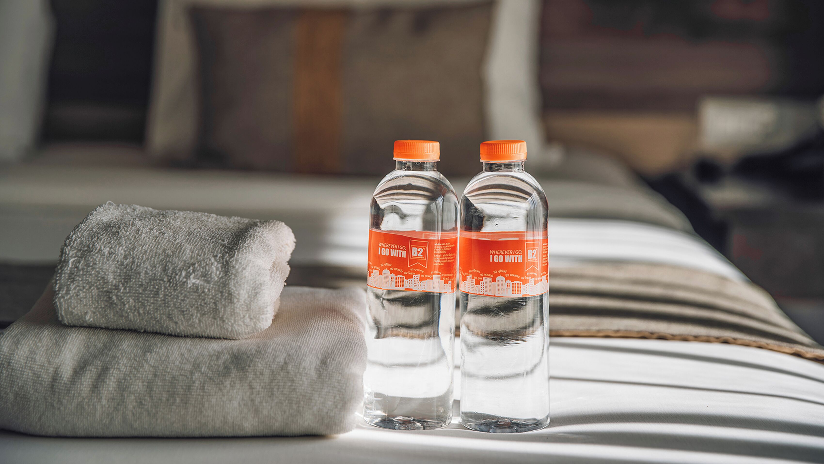 Two bottles of water on a bed with a folded towel.