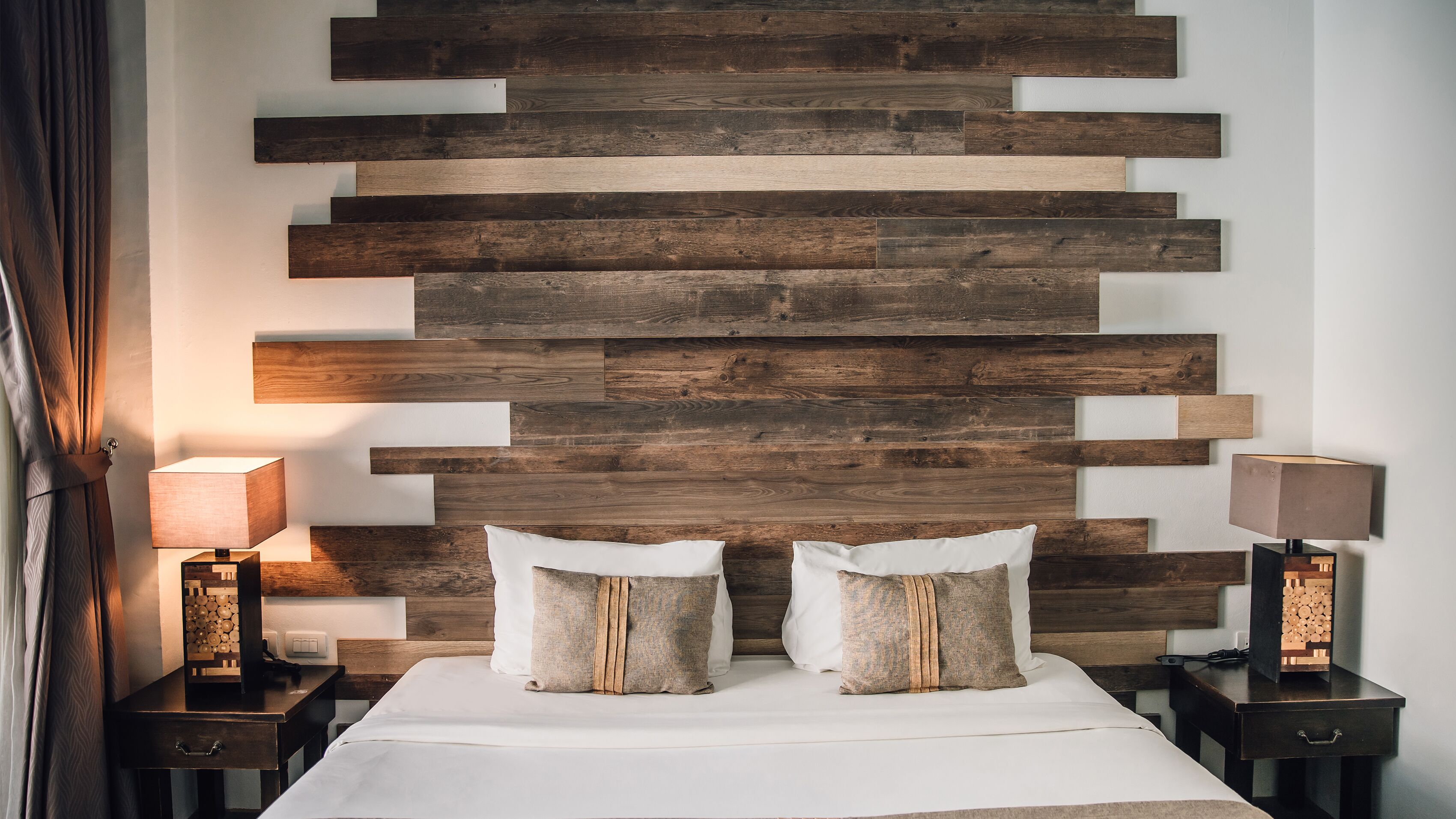 A bedroom with a wooden headboard, two bedside tables with lamps, a bed with white linens, and two decorative pillows.
