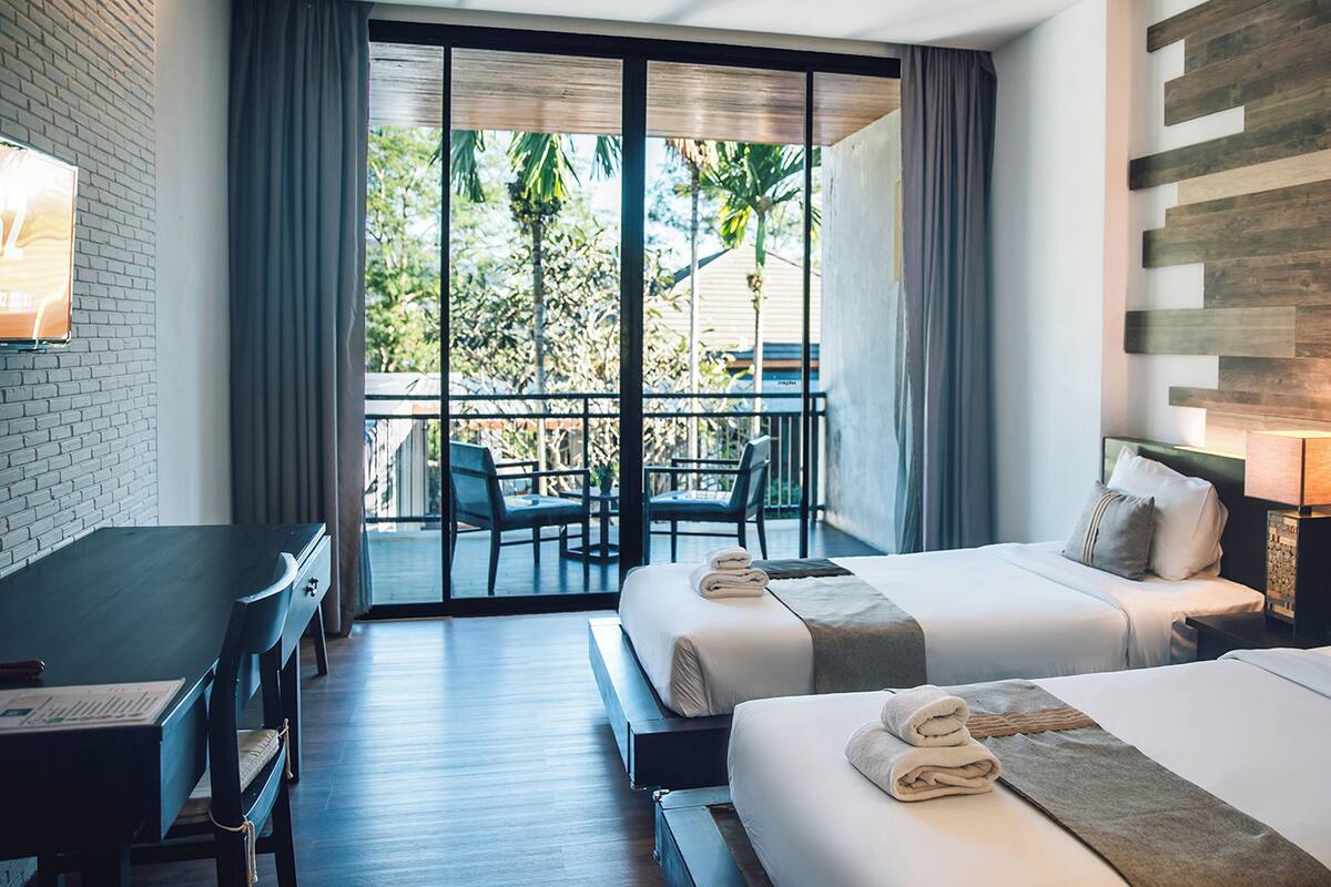 A hotel room with two beds, a desk, a chair, and a balcony with a table and chairs.