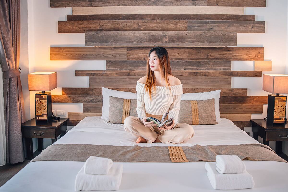 A hotel room with a wooden headboard, two bedside tables with lamps, a bed with white linens, and two towels on the bed.