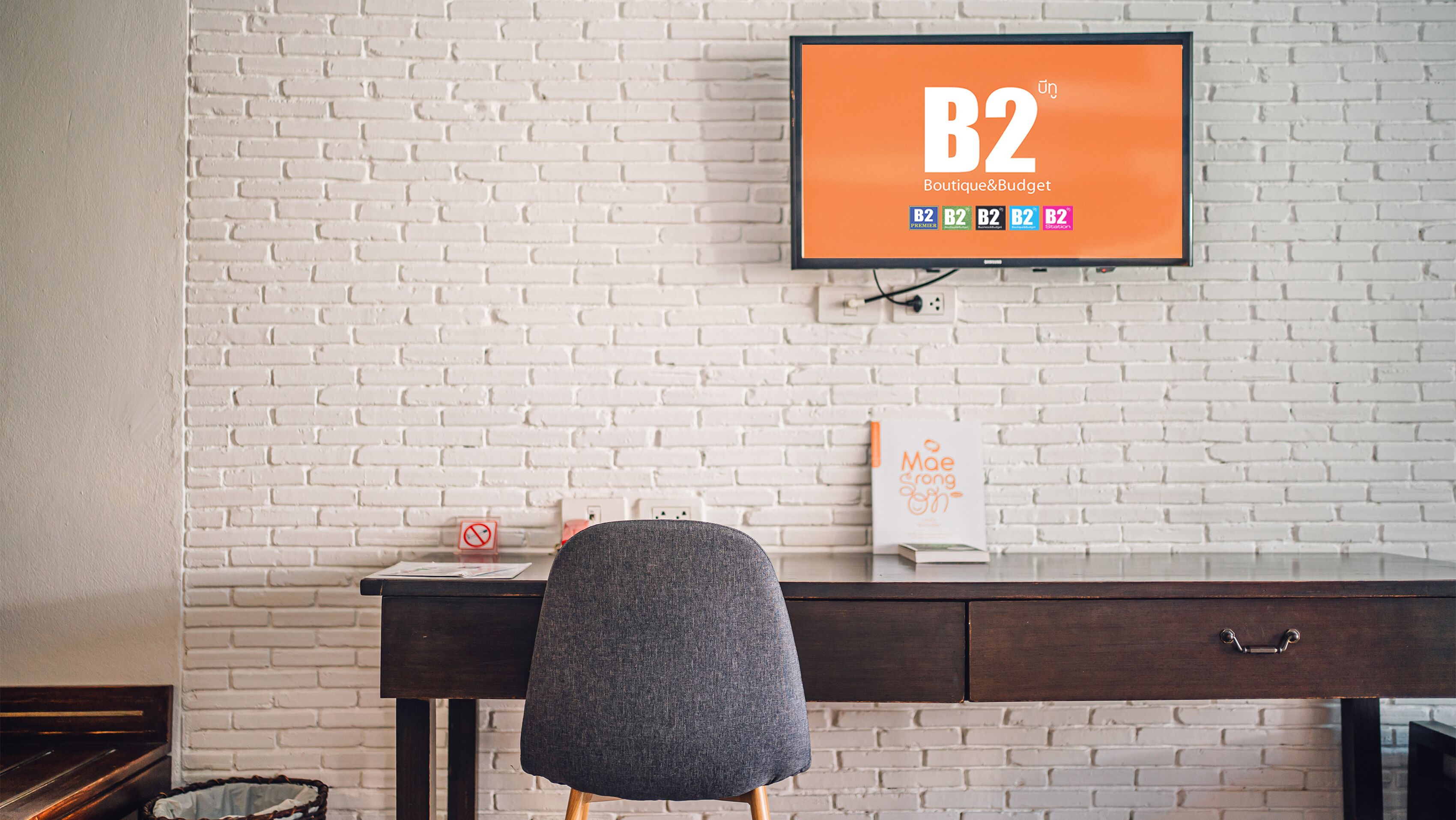 A workspace with a white brick wall, a desk with a chair, and a TV displaying 'B2 Boutique&Budget'.