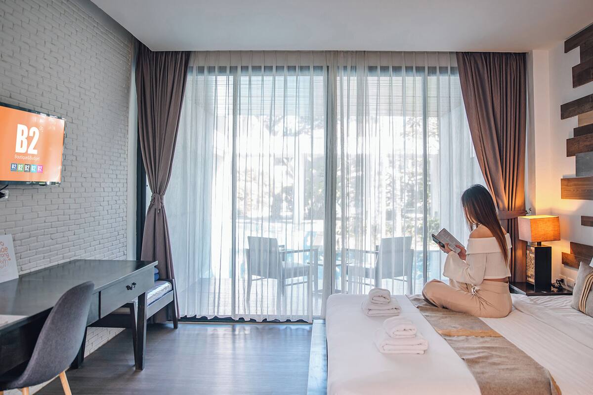 A hotel room with a bed, a desk, a chair, a TV, and a window with curtains.