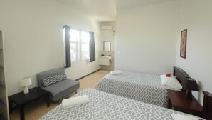 A hotel room with two beds, a sofa, a desk, a chair, a window with curtains, and a ceiling fan. - Talofa Inn (Apia)