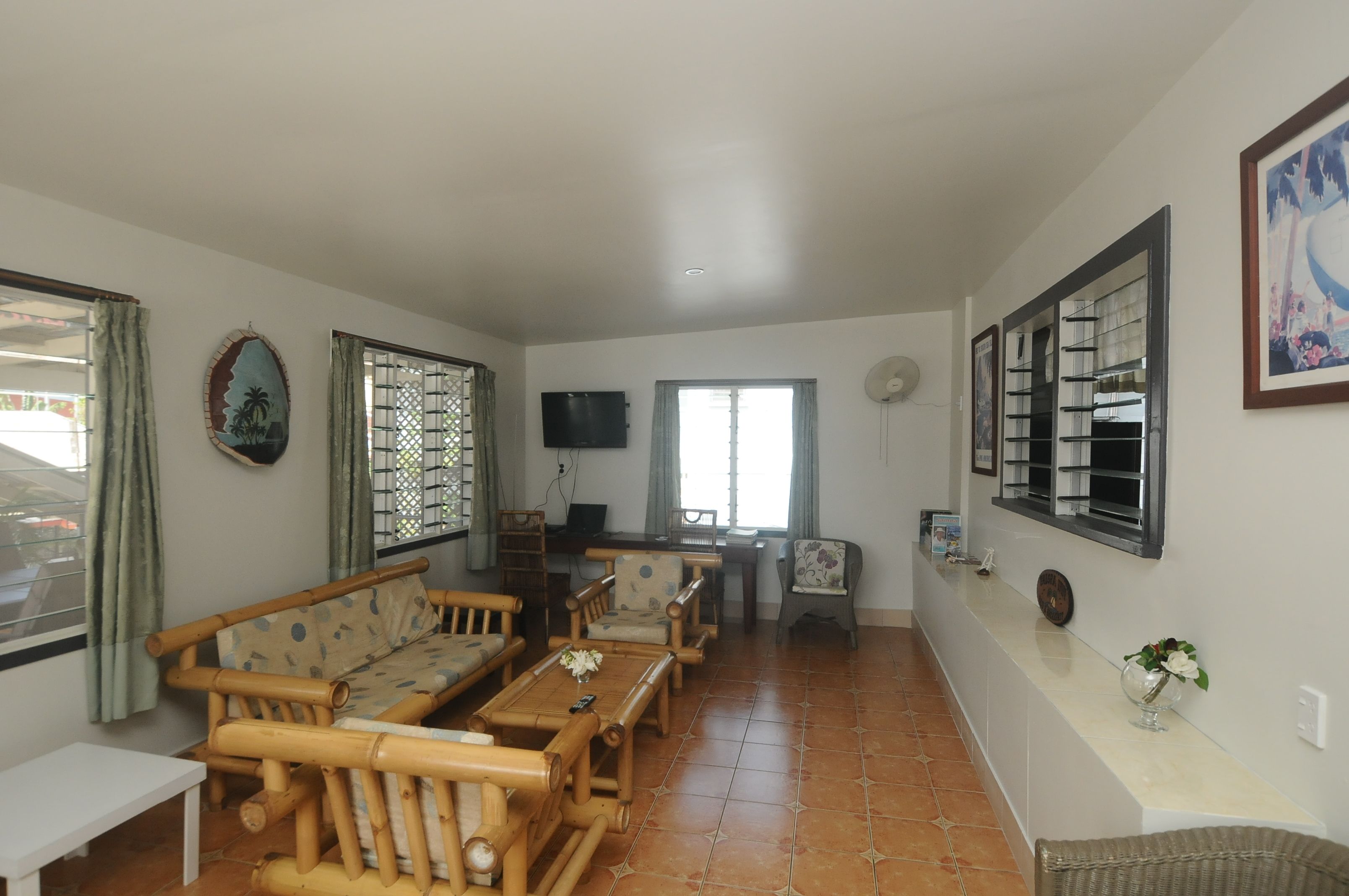 A living room with a sofa set, a dining table, and a TV mounted on the wall.