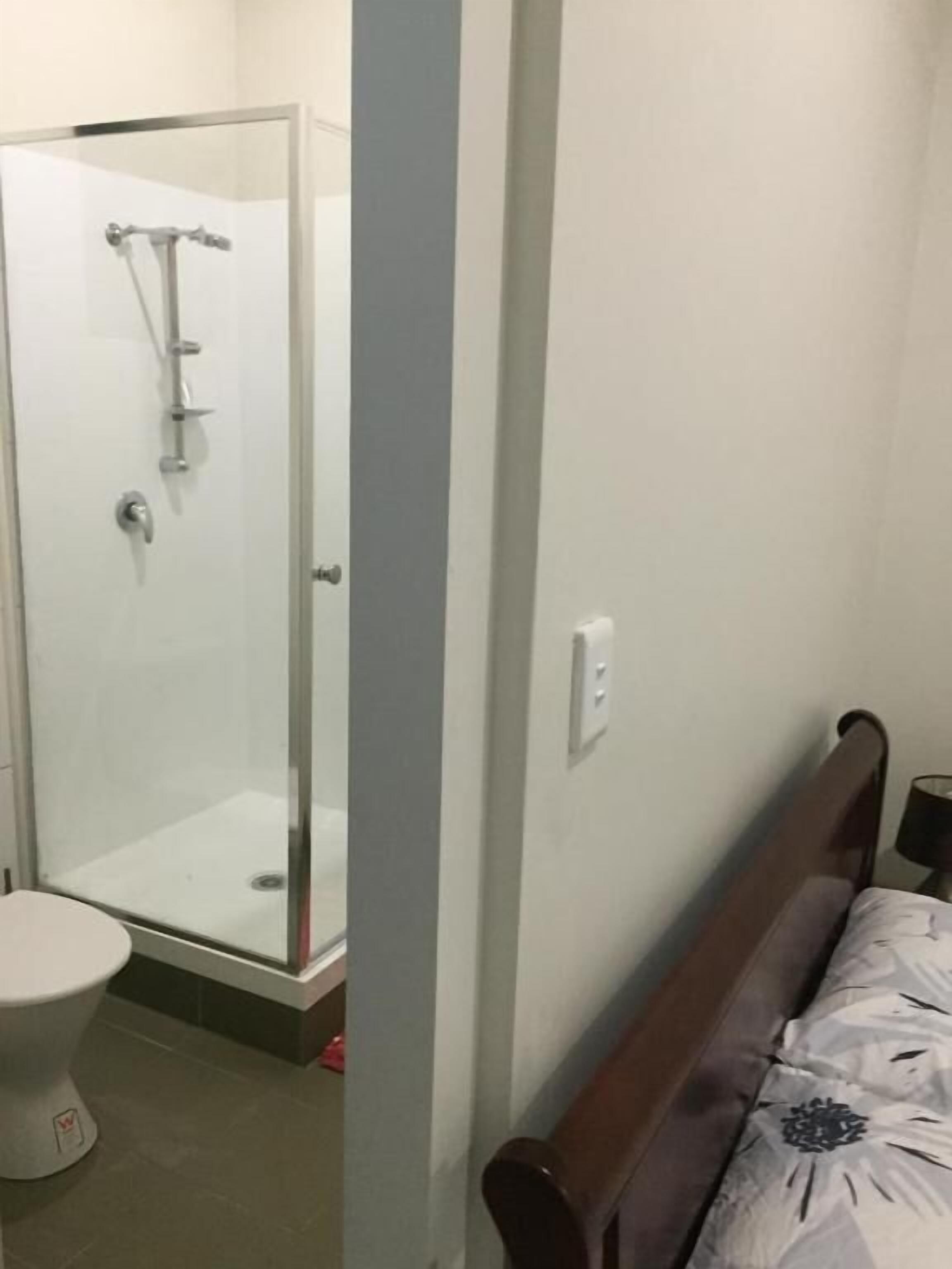 Une salle de bain avec une douche à parois de verre, des toilettes et un lit recouvert d’une couvre-lit à motifs.