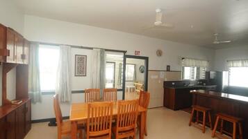 A spacious living area with a wooden dining table and chairs, a kitchen with a black countertop, and a ceiling fan.