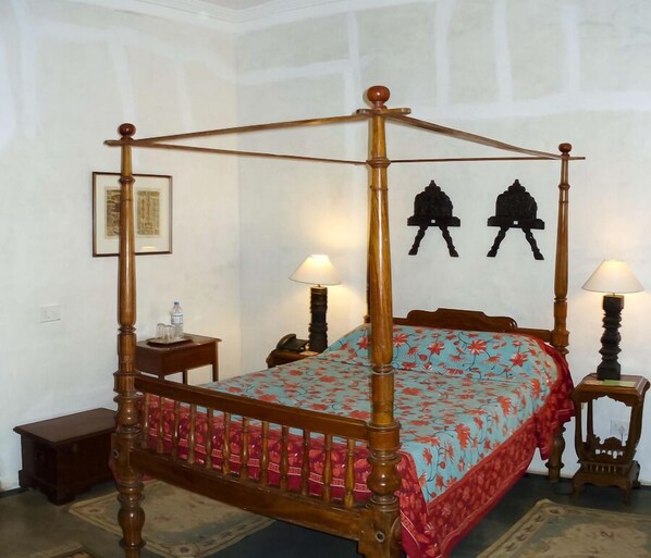 A four-poster bed with a floral bedspread, two bedside tables, and wall-mounted lamps. - Hotel De L'Orient Pondicherry (Puducherry)