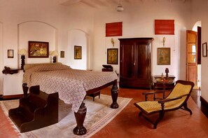A traditional room with a bed, a wooden chair, a cabinet, and artwork on the walls. - Hotel De L'Orient Pondicherry (Puducherry)