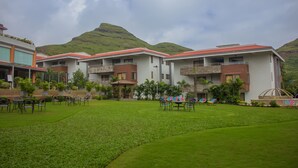 A hotel with multiple buildings, a well-maintained lawn, and a mountainous backdrop. - Club Mahindra Hatgad (Nashik)