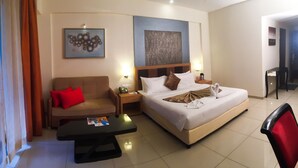 A hotel room with a bed, a sofa, a nightstand, a table, and two wall art pieces. - Club Mahindra Hatgad (Nashik)