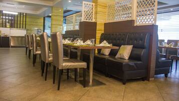 Un restaurante con una larga mesa dispuesta para comer, asientos acolchados y un separador decorativo.