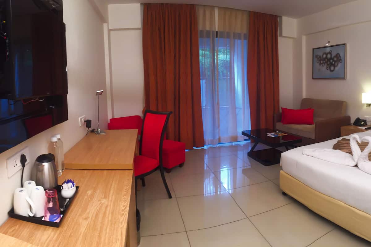 A hotel room with a bed, a desk with a chair, a sofa, a coffee table, and a TV.