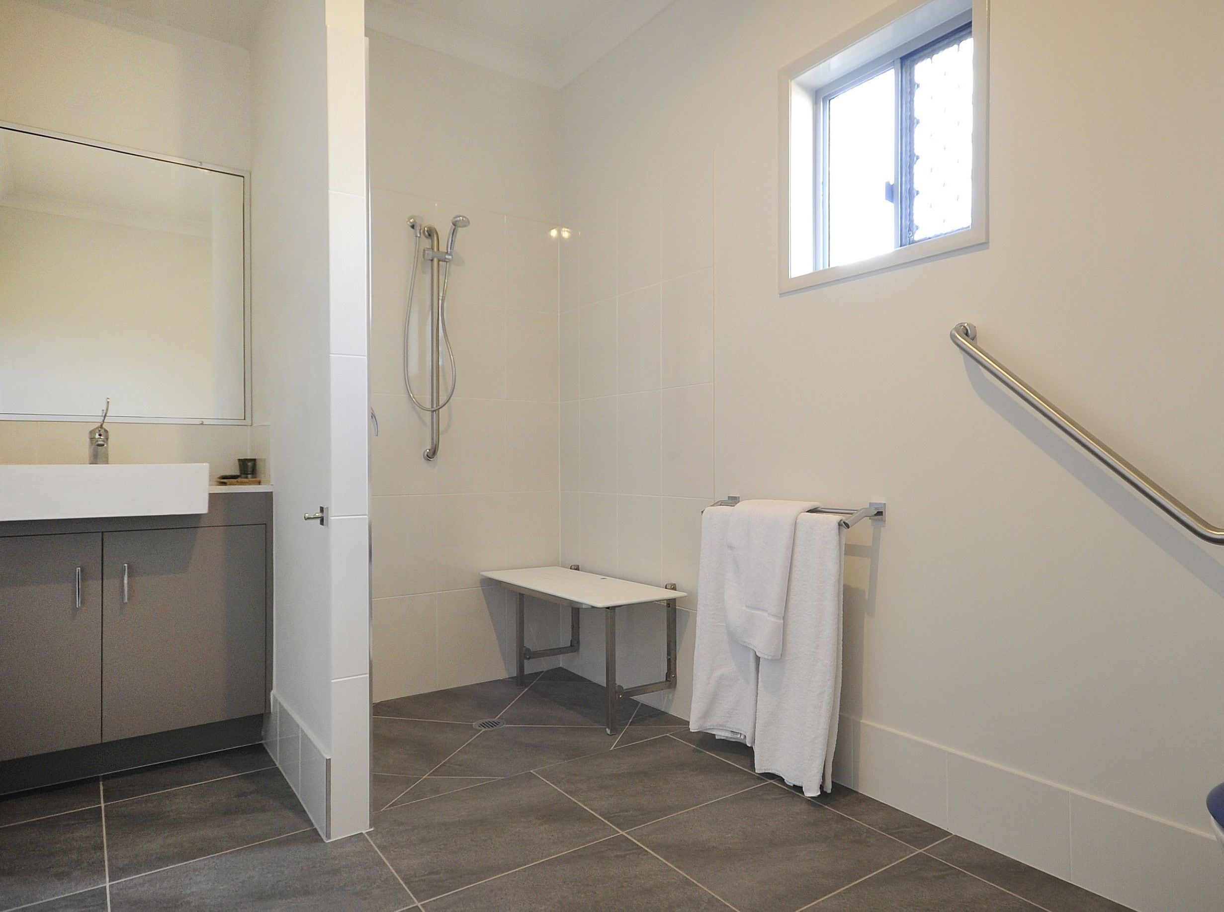 A bathroom with a shower, a sink, a mirror, and a window.