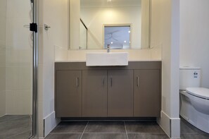 A modern bathroom with a white sink, beige cabinets, and a glass shower enclosure.