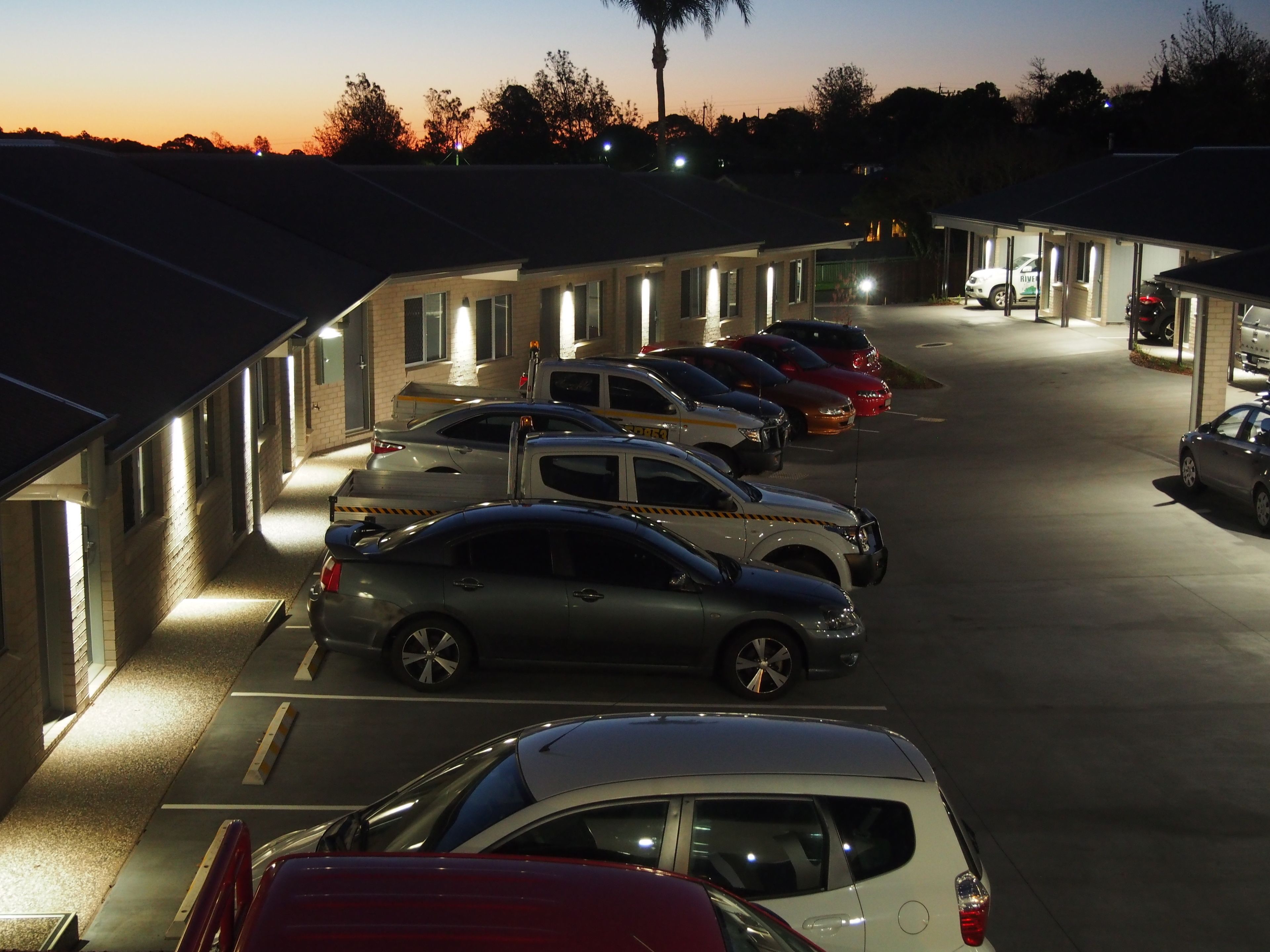 A parking lot with several cars parked in front of a motel with multiple rooms.