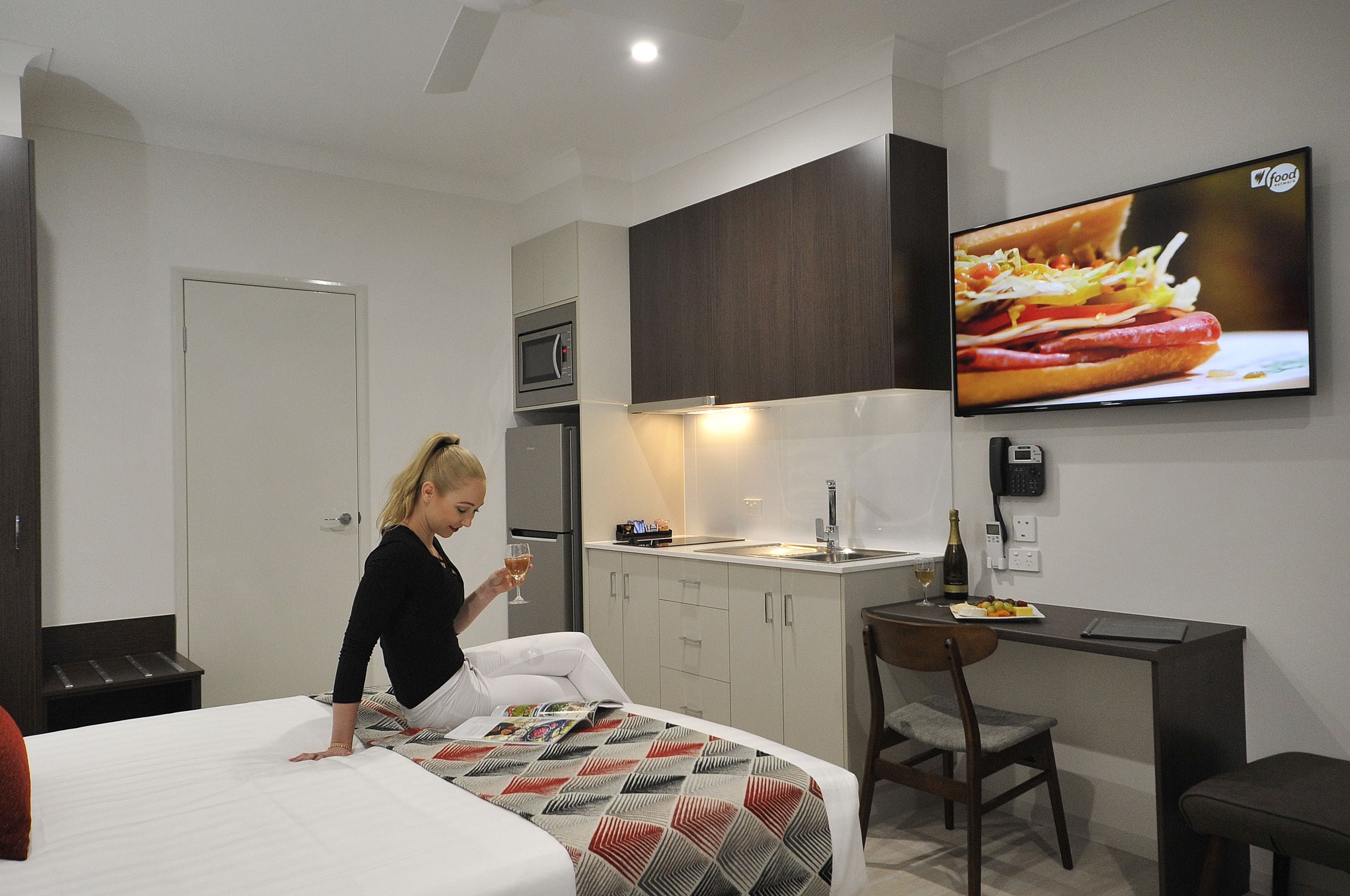 A hotel room with a bed, a desk, a TV, a microwave, and a minibar.