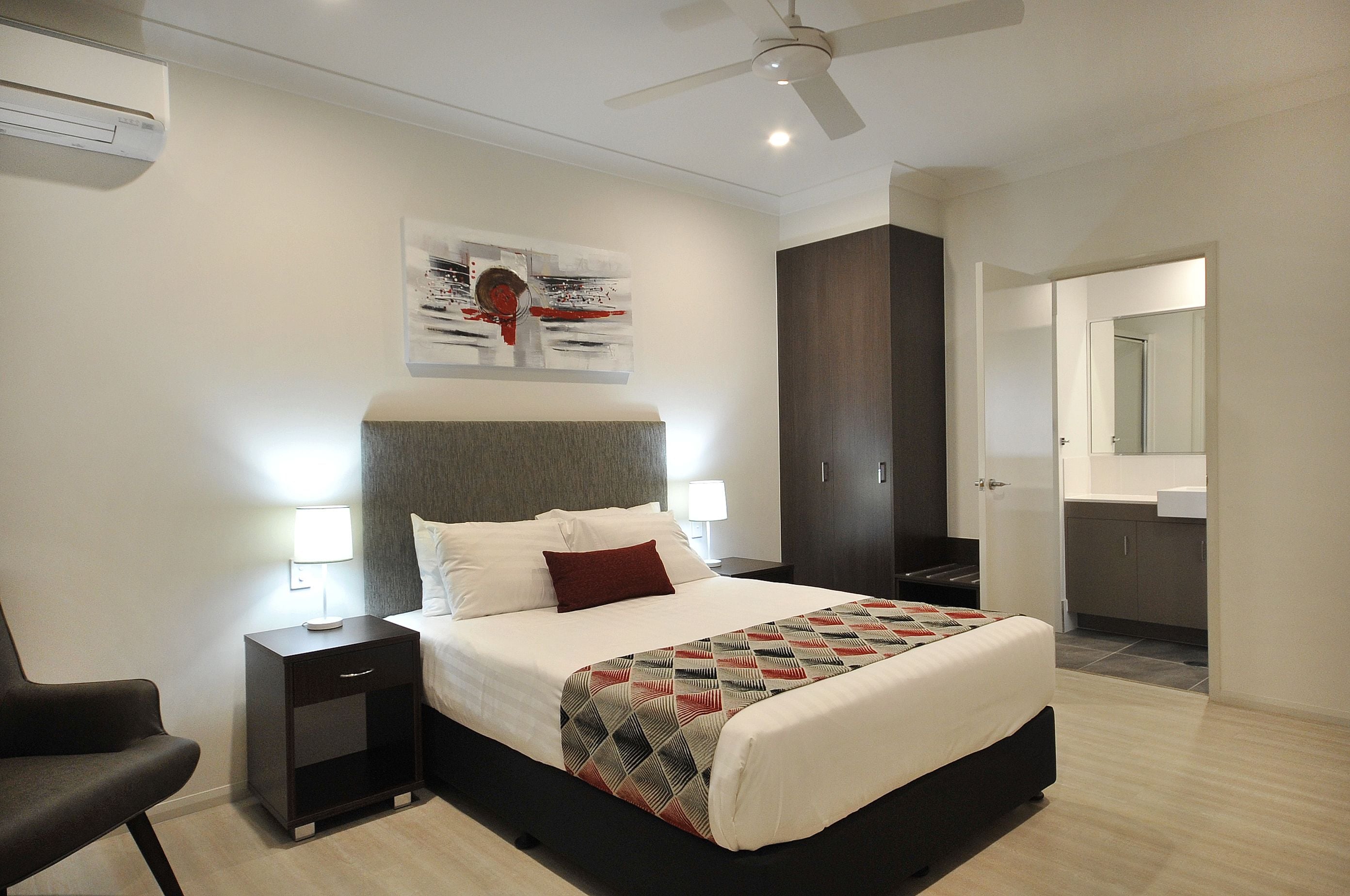 A modern hotel room with a large bed, bedside tables, a ceiling fan, and a bathroom visible through an open door.