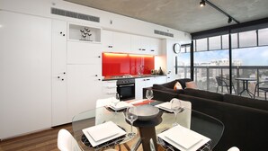 A modern kitchen with white cabinets, a red backsplash, and a dining area with a glass table and black sofa. - StayCentral - NGV Arts Centre Retreat (Southbank)