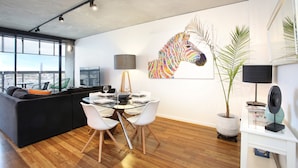 A modern living room with a glass dining table, white chairs, a black sofa, and a large zebra mural on the wall. - StayCentral - NGV Arts Centre Retreat (Southbank)