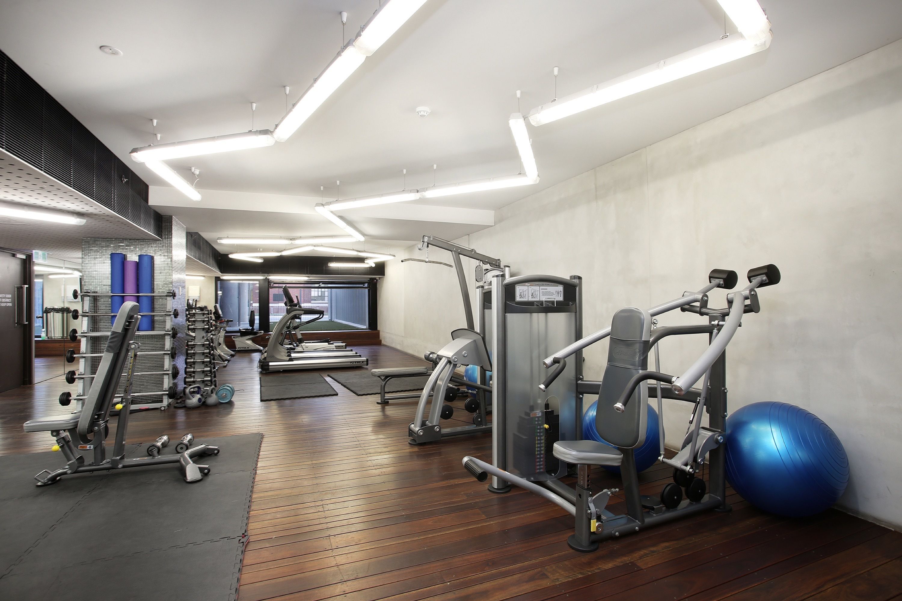 A gym with various exercise equipment, wooden flooring, and a large mirror.