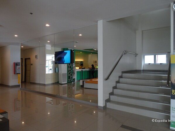 A modern lobby with a staircase, a reception desk, and a large flat-screen TV. - Go Hotels Lanang - Davao (Davao)