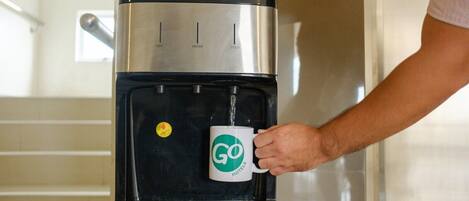 A person filling a mug from a water dispenser with a "HOT," "WATER," and "COLD" button panel.