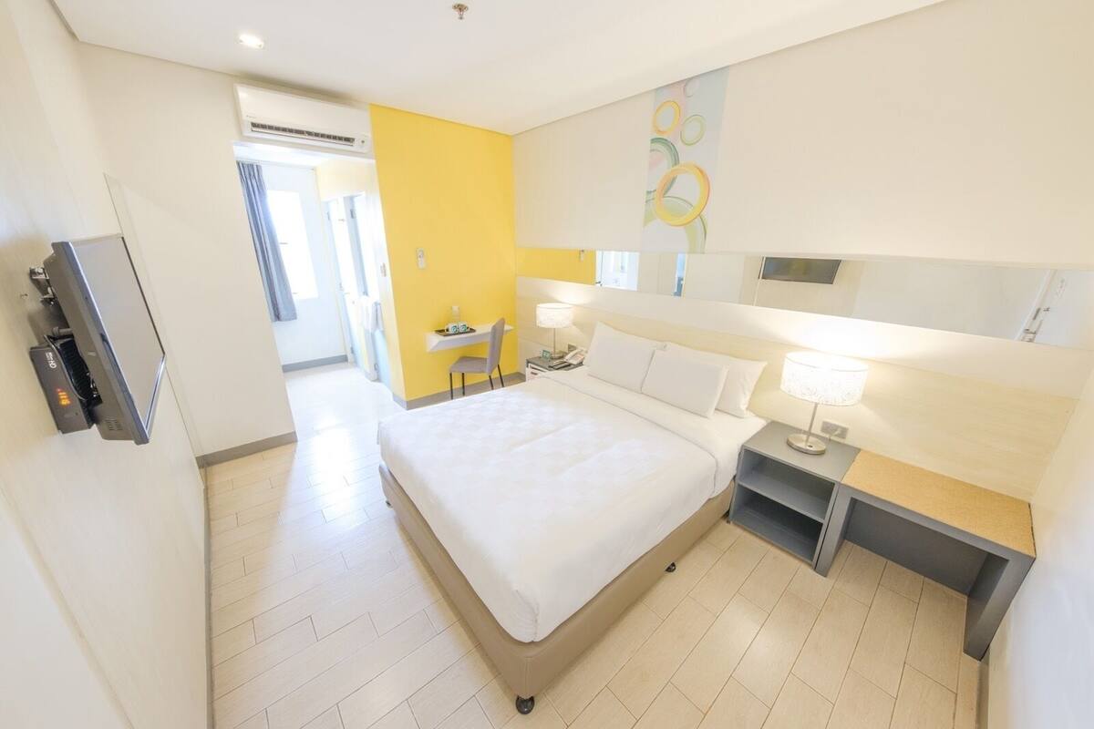 Ein Hotelzimmer mit Bett, Nachttisch, Lampe und Schreibtisch mit Stuhl.