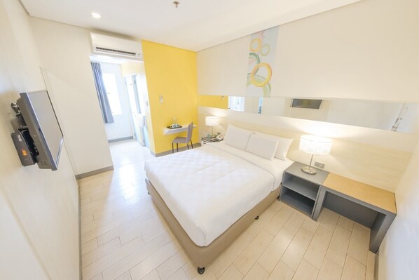 A hotel room with a bed, bedside table, lamp, and a desk with a chair.