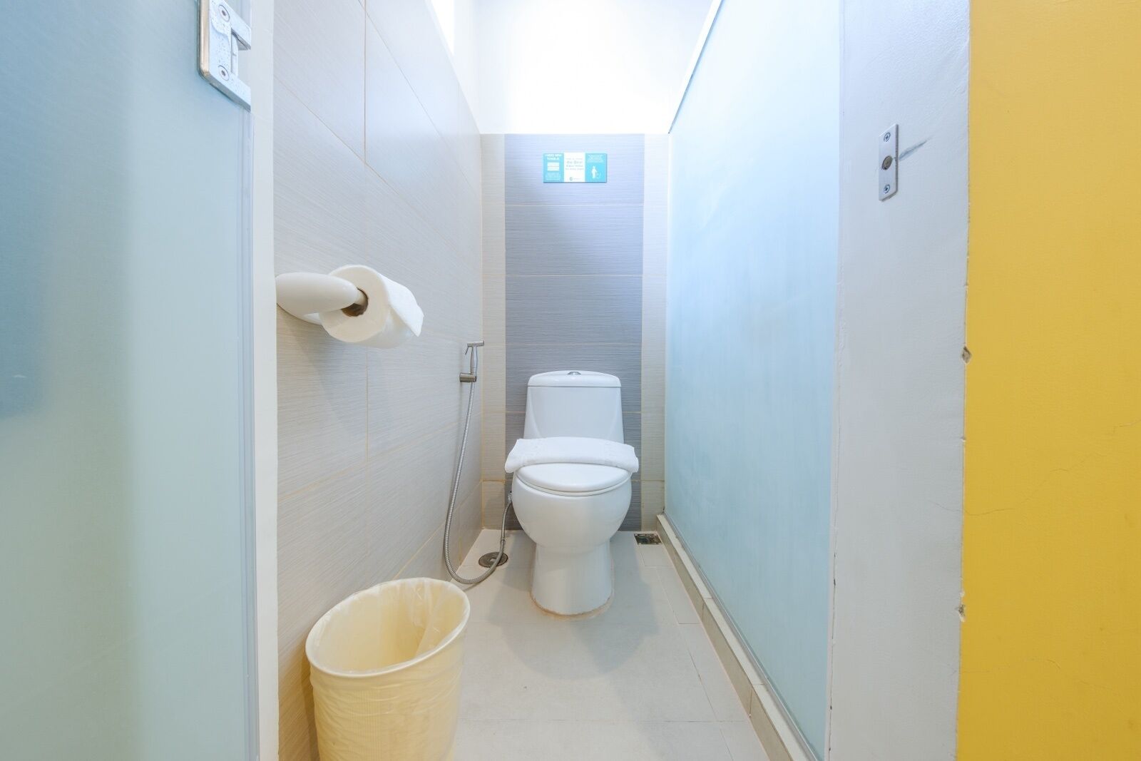 A narrow bathroom with a toilet, a hand dryer, and a trash bin.