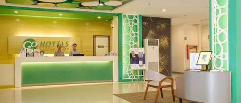 A hotel reception area with a green and white color scheme, a reception desk, and a modern ceiling design.