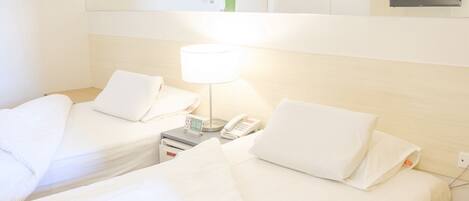 A hotel room with two single beds, a bedside table with a lamp, a phone, and a small cabinet above the beds.