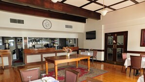 Un comedor con una mesa de madera dispuesta para una comida, una zona de bar con un reloj y un televisor en la pared.