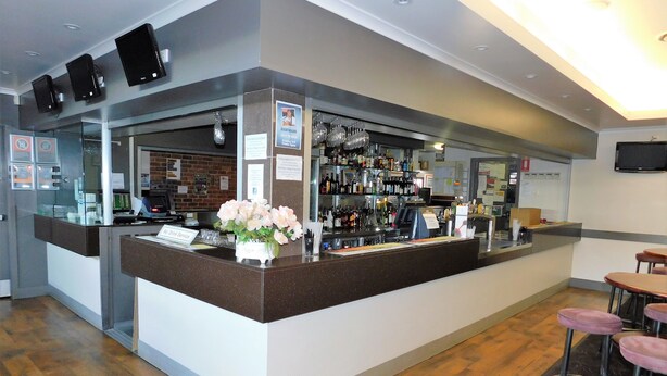 Zona de bar con mostrador, taburetes y una exhibición de botellas y vasos.