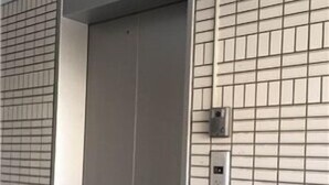 A modern elevator with a metallic finish, a control panel on the wall, and a tiled wall with a grid pattern. - Peace International hotel Ichinomiya (Ichinomiya)