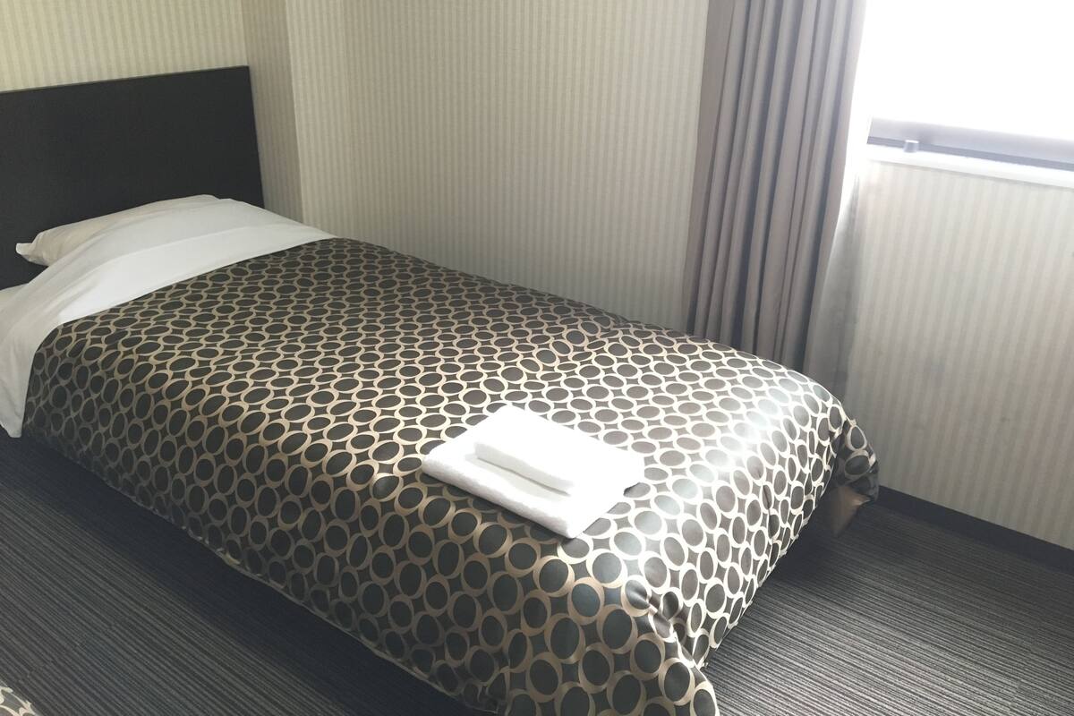 Une chambre d’hôtel avec un lit, une tête de lit, une fenêtre avec des rideaux et un sol recouvert de moquette.