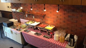 A buffet setup with various food items and condiments, a checkered tablecloth, and a brick wall background. - Peace International hotel Ichinomiya (Ichinomiya)