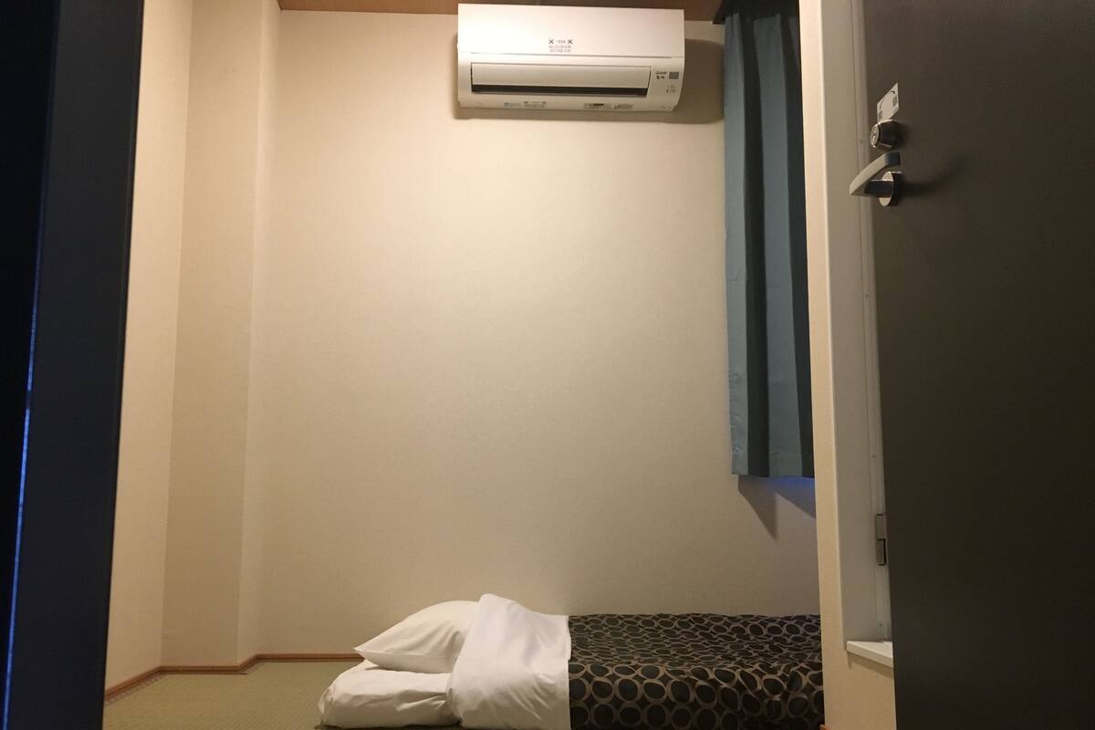 Une chambre d’hôtel avec un lit, un climatiseur fixé au mur et une porte dotée d’une poignée.