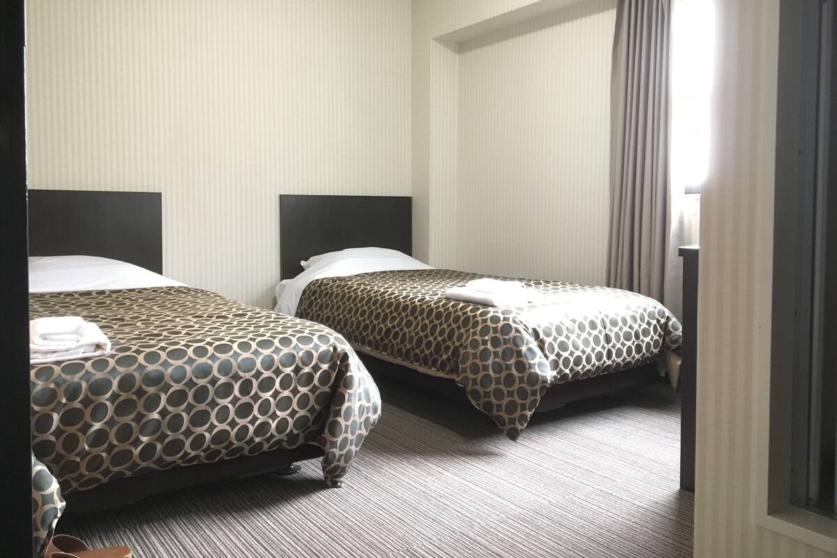 Une chambre d’hôtel avec deux lits, une fenêtre avec des rideaux et un sol recouvert de moquette.