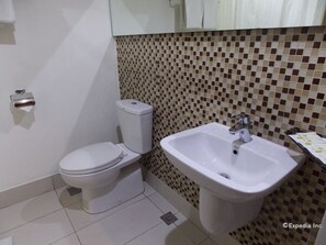 Une salle de bain avec des toilettes et un lavabo, un sol carrelé et un mur orné d’un motif à carreaux.