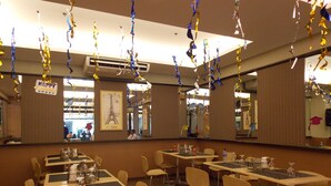 Un área de comedor con mesas y sillas, decorada con serpentinas y un cartel que dice 'Happy Graduation'.
