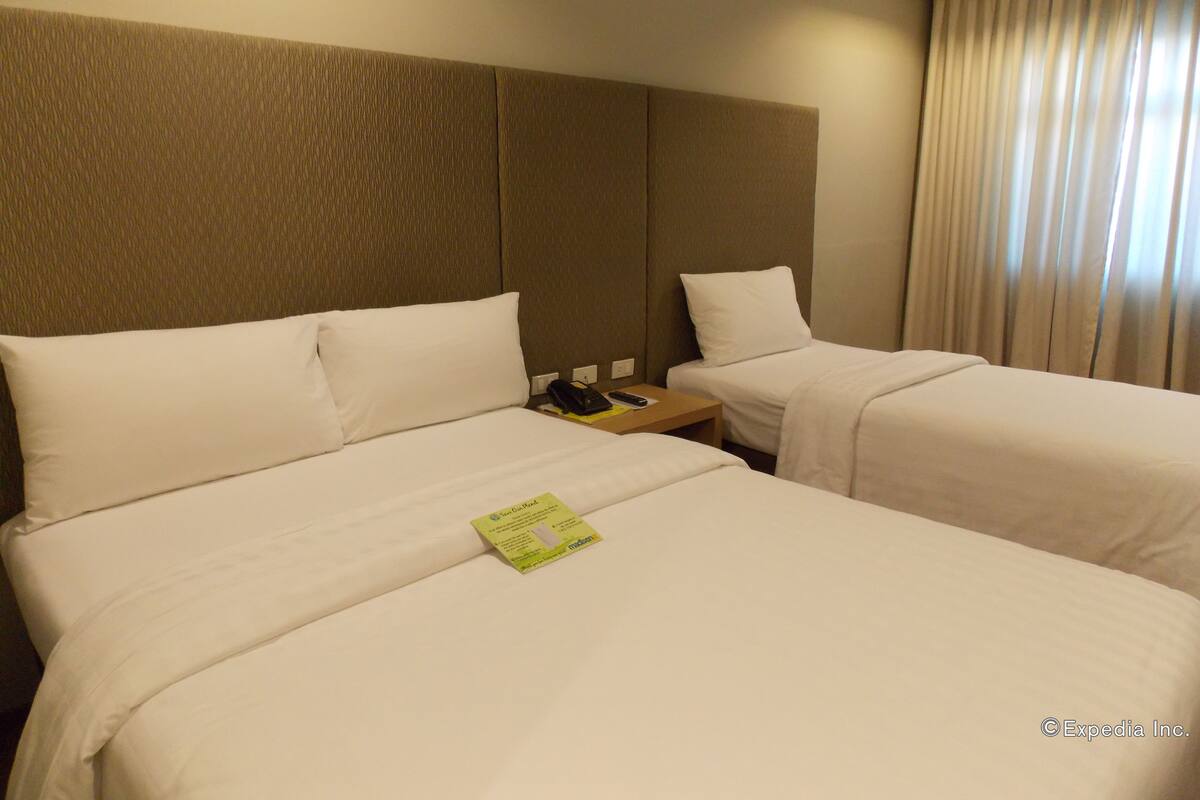 A hotel room with two beds, a headboard, a bedside table with a phone, and a curtain.