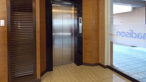 Un ascensor en un pasillo con paneles de madera y suelo de baldosas.