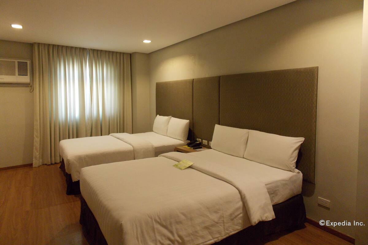 A hotel room with two beds, a nightstand, and a window with curtains.