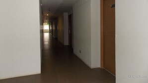 Un largo pasillo estrecho con paredes blancas y piso marrón. Hay puertas a la derecha y una señal de salida al final.