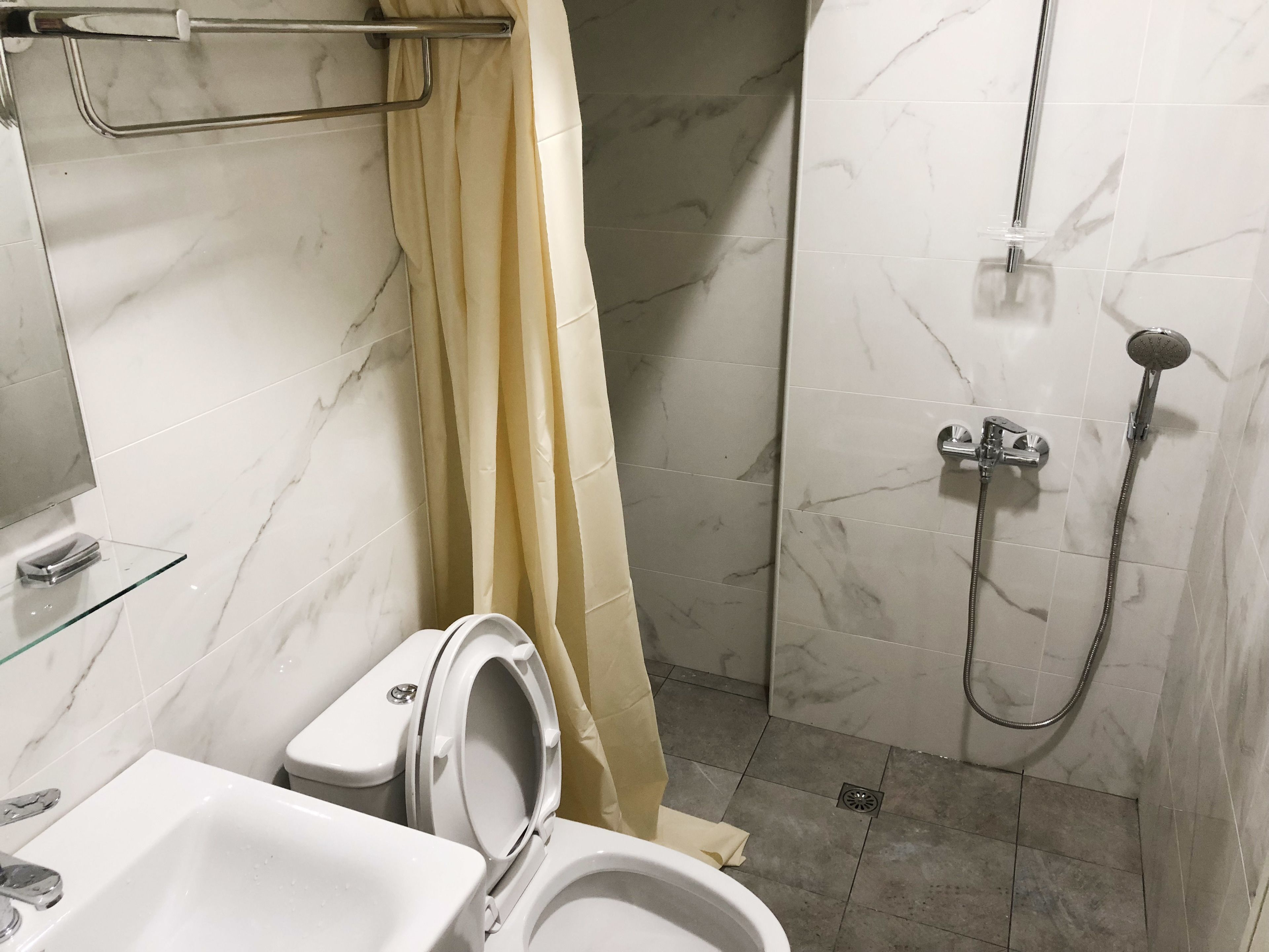 A bathroom with a toilet, sink, shower, and marble walls.