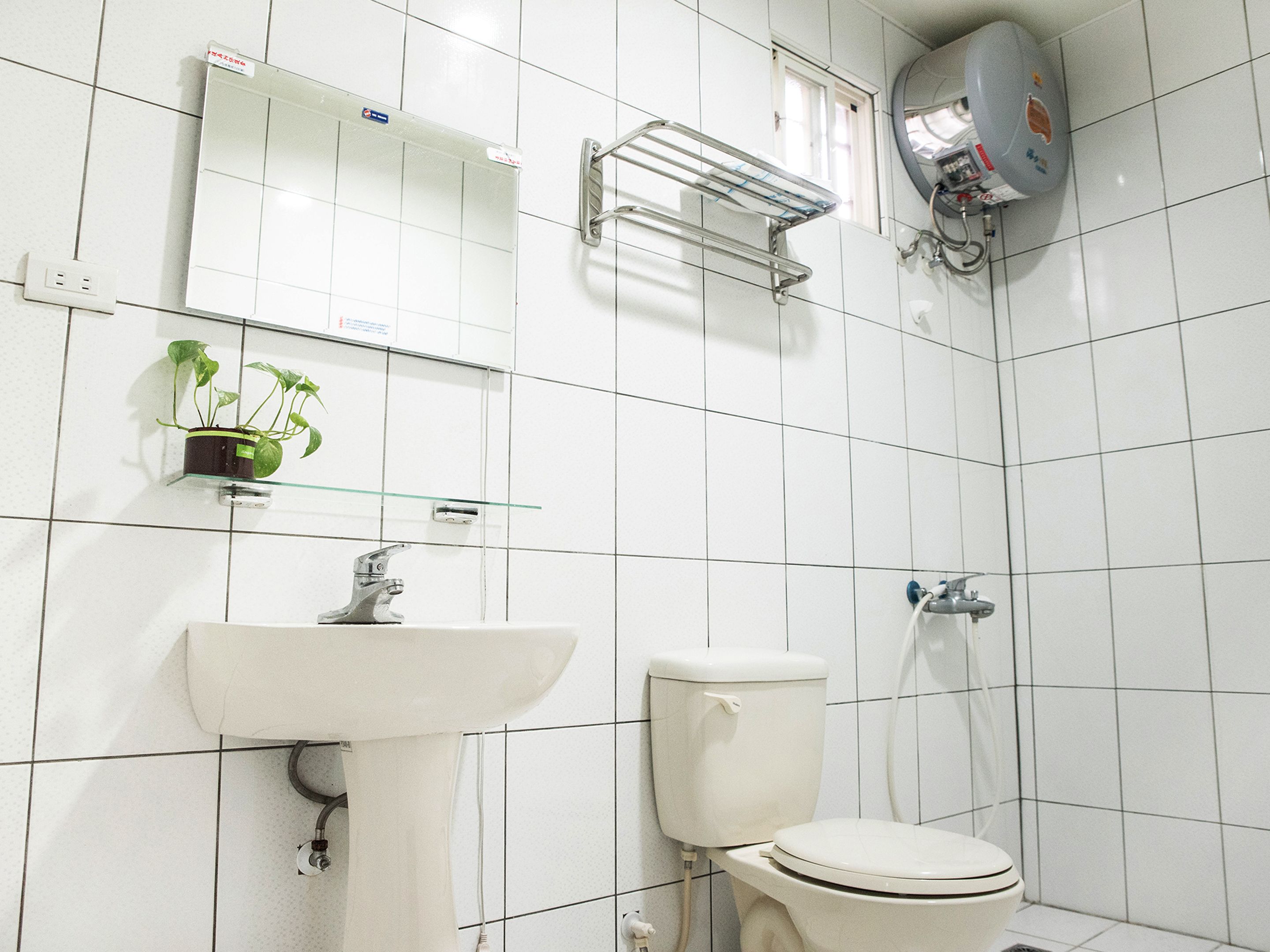 Kylpyhuone, jossa on valkoinen pesuallas, wc ja lasihylly, jonka päällä on ruukussa oleva kasvi.