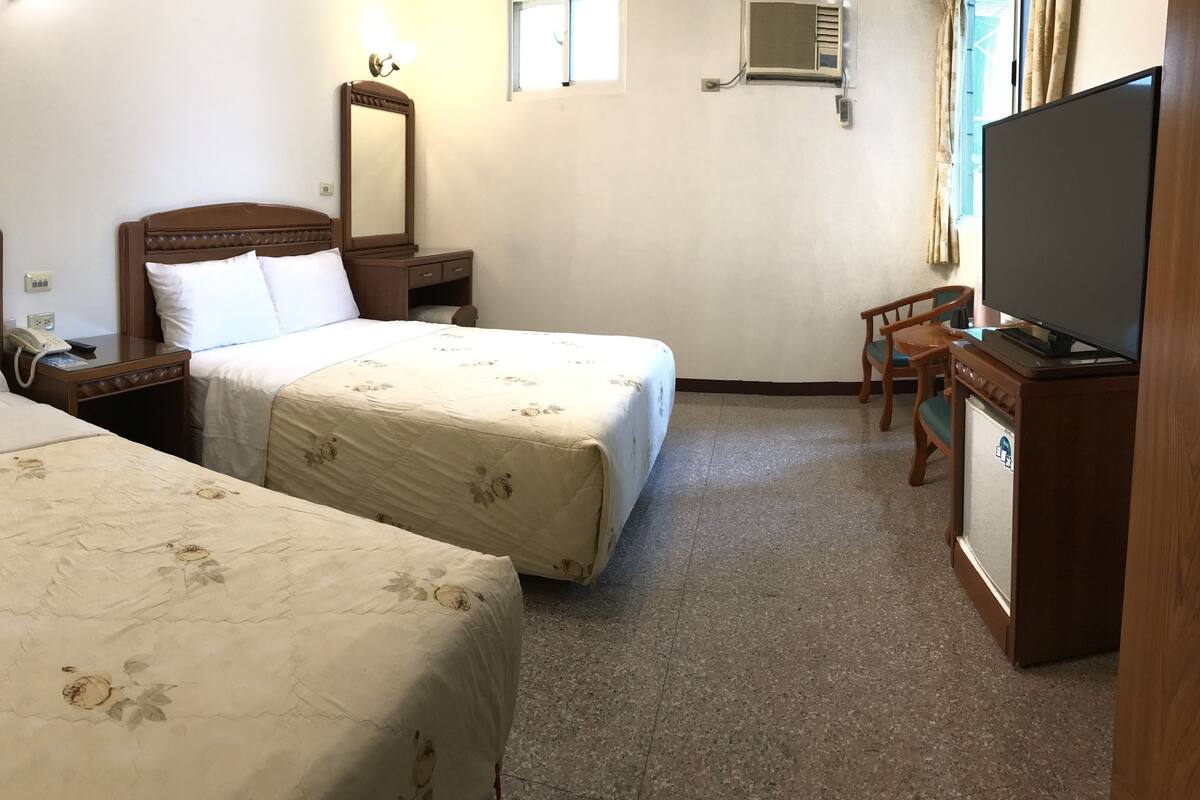 A hotel room with two beds, a TV, a desk, and a chair.